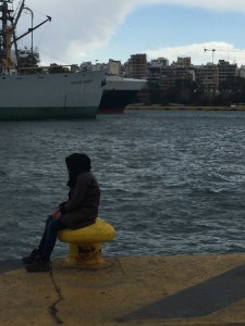 Een jong meisje uit SyriÃ« staart doelloos voor zich uit op de kade. Op de achtergrond, de Hellas Liberty.